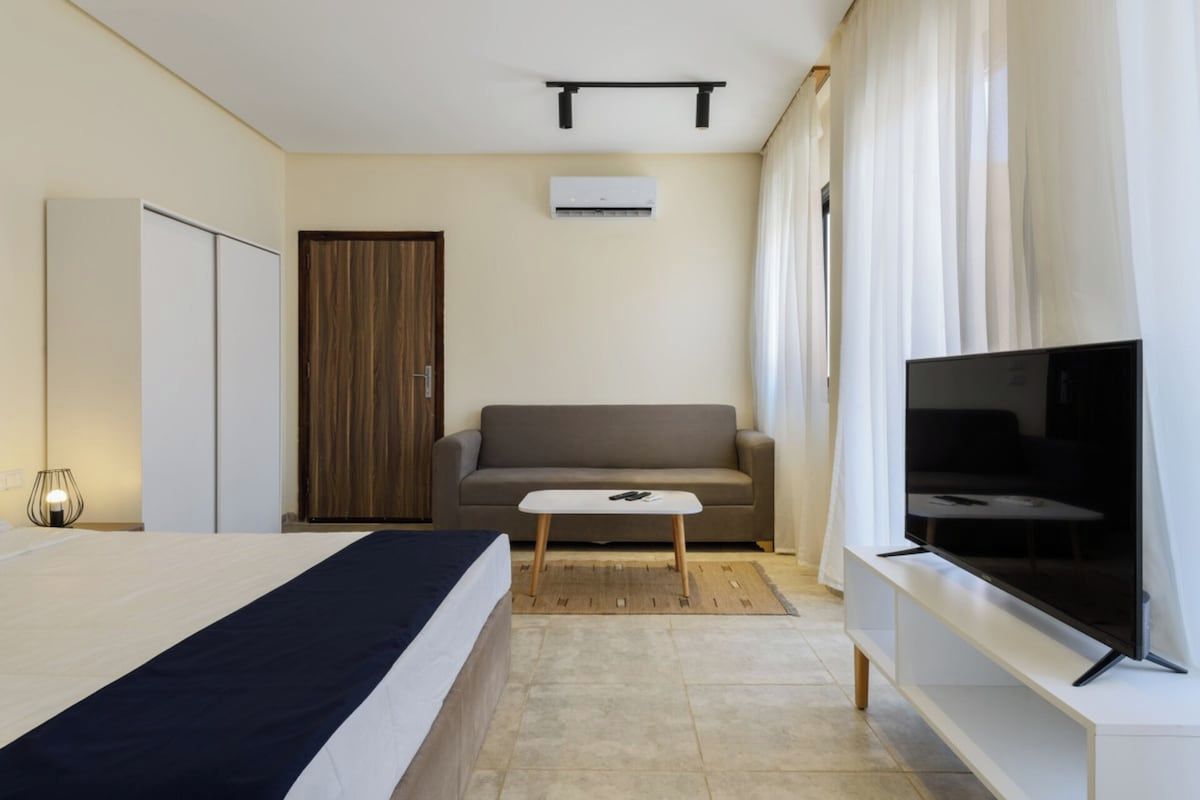 A modern hotel room with a bed, a sofa, a TV, and a wardrobe.