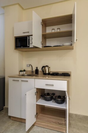 A compact kitchenette with a microwave, kettle, and pots on the counter. - Nomads Residence (Cairo)