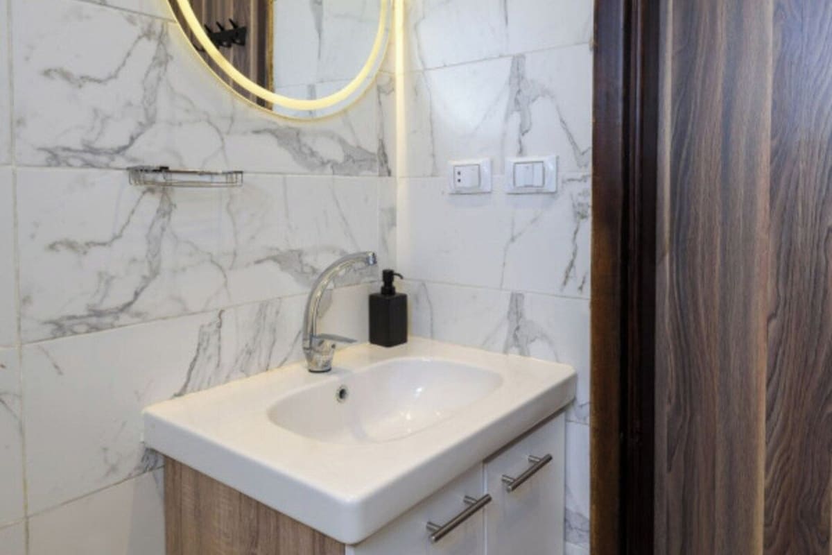 A bathroom with a marble wall, a white sink, wooden cabinets, and a wooden door.