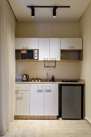 Una cocina compacta con armarios blancos, un microondas, un hervidor y un refrigerador.