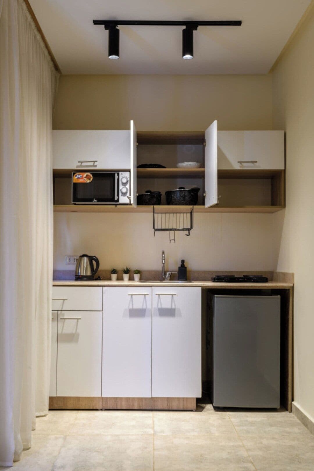 Cocina compacta con armarios blancos, microondas, hervidor y refrigerador.