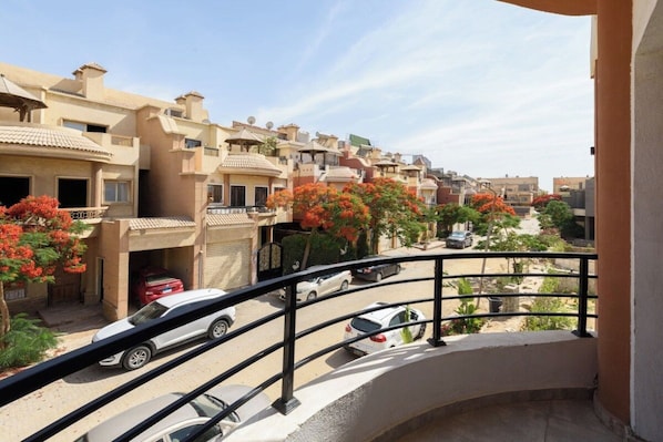 A residential area with multiple-story buildings, a balcony with a railing, and parked cars.