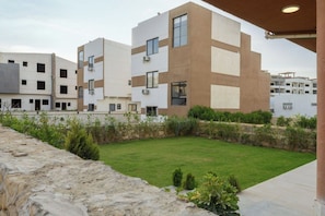 A modern building with multiple floors and balconies, surrounded by a well-maintained lawn and stone walls.