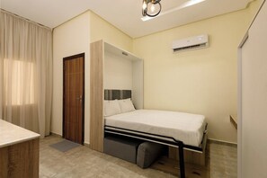 Quarto compacto com cama, guarda-roupa e ar condicionado.