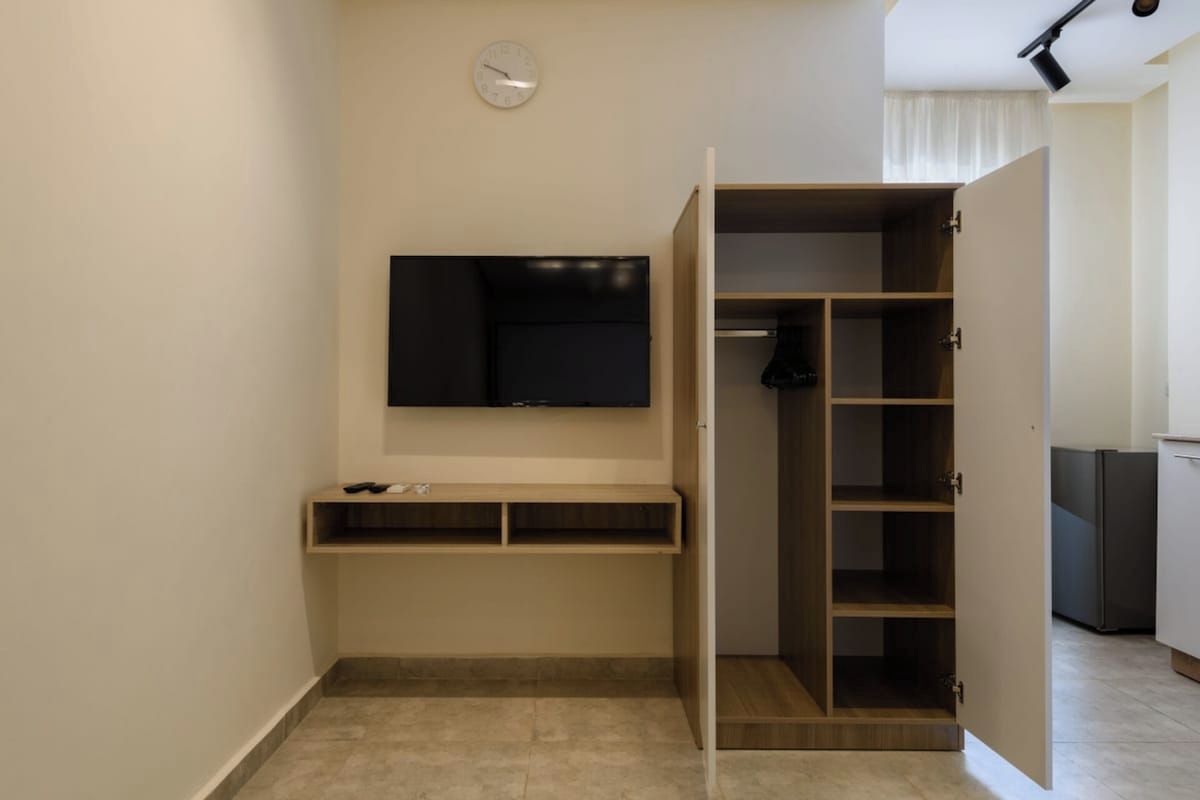 A compact room with a built-in TV, a small shelf, and a wardrobe with multiple compartments.