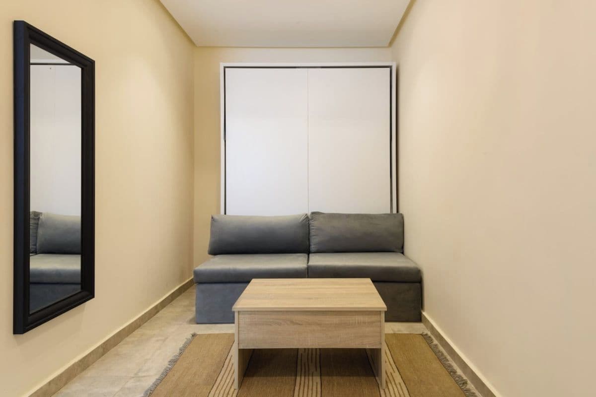 A small, narrow room with a sofa, a coffee table, a mirror, and a wardrobe.