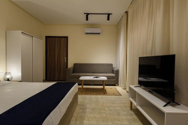 Quarto de hotel com cama, sofá, televisão e guarda-roupa.