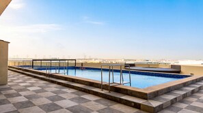 A rooftop swimming pool with clear blue water, a tiled deck, and a view of the city skyline. - 1BR near Expo City with Pool, Gym & Basketball (Jebel Ali)