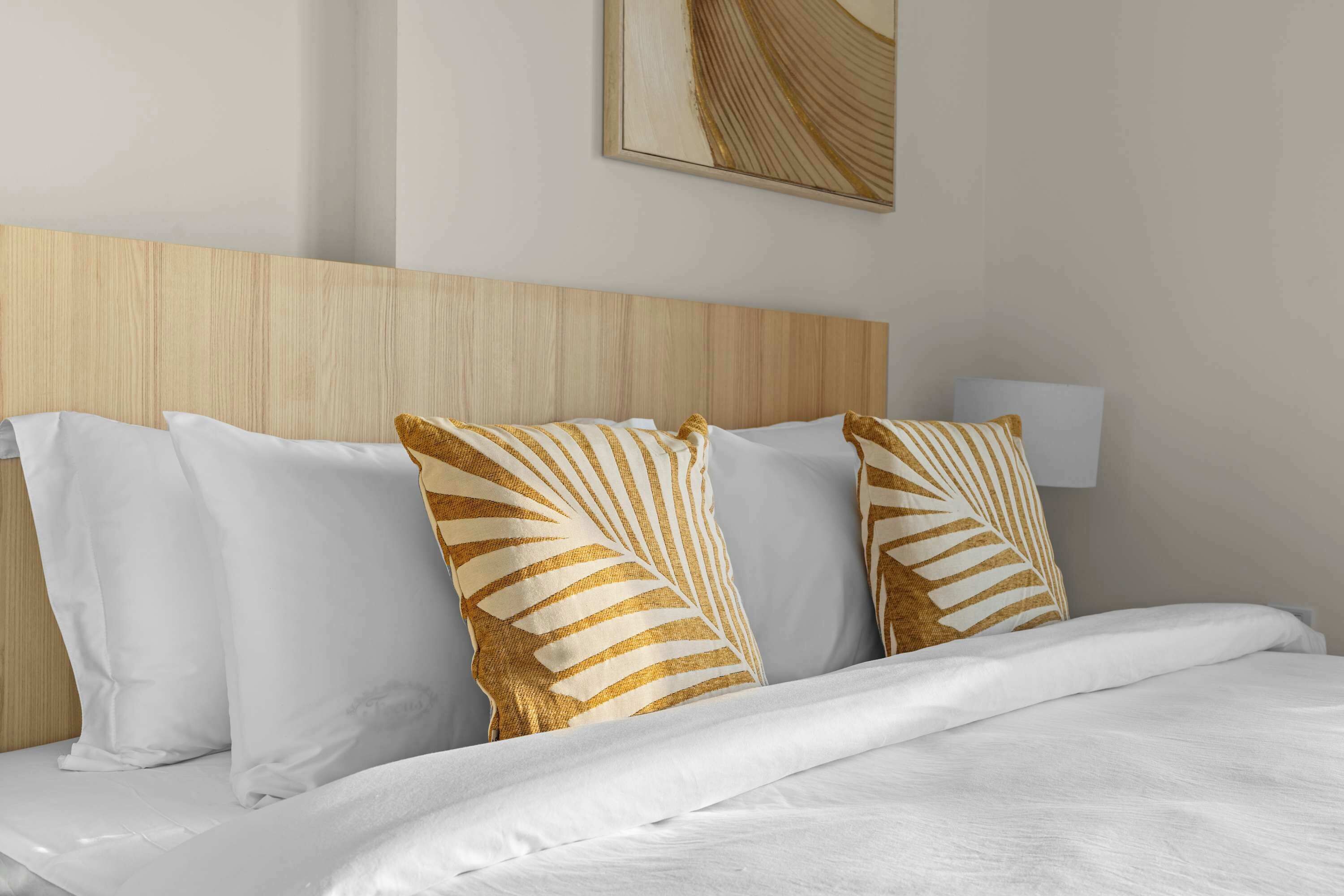 Una cama bien hecha con ropa blanca y almohadas decorativas con un estampado de hojas.