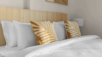 Una cama bien hecha con ropa blanca y almohadas decorativas con un estampado de hojas.