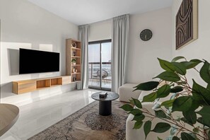 Ein modernes Wohnzimmer mit Flachbildfernseher, Holzregalen, einem runden Couchtisch und Blick auf die Stadt durch große Fenster.