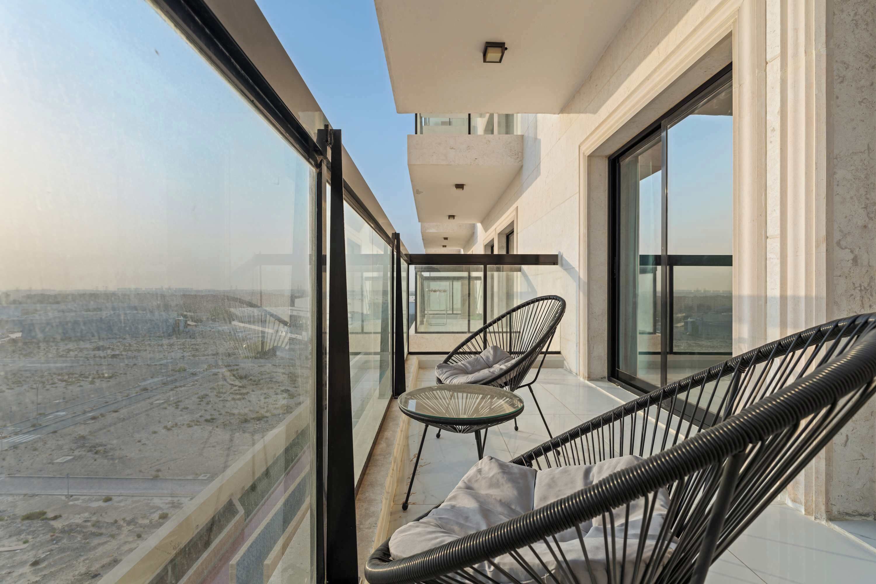 Ein Balkon mit Glasgeländer, zwei Korbstühle und einem kleinen Tisch.