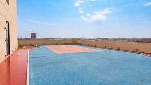Un court de tennis situé sur le toit d’un immeuble, avec un ciel dégagé et des bâtiments visibles au loin.