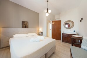 A bedroom with a large bed, a bedside table with a lamp, a wooden wardrobe, a mirror, and a wall-mounted artwork. - The San Villa with Caldera Sea View and Private Hot Tub in Oia (Oia)