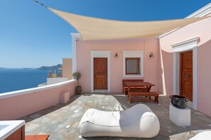 Ein Balkon mit Meerblick, einem Holztisch, einem weißen Pouf und einer Topfpflanze.