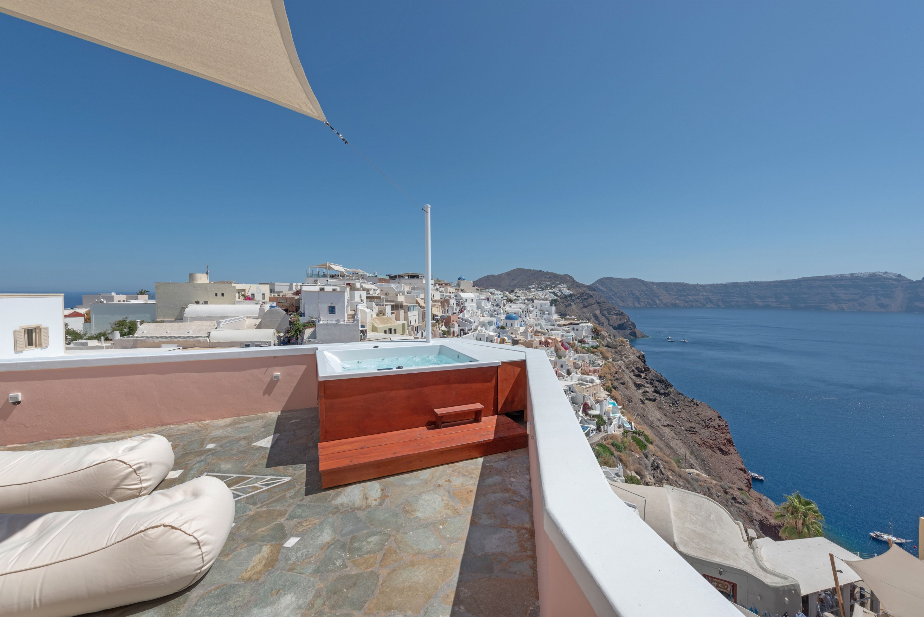 Terraza en la azotea con jacuzzi, zona de estar y vistas a un pueblo costero y el mar.
