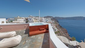 Terraço no telhado com hidromassagem, área de estar e vista para uma cidade costeira.