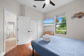Ein Schlafzimmer mit Bett, Fernseher, Fenster mit Blick und Deckenventilator.