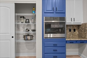 Eine Küche mit weißen Schränken, einer blauen Arbeitsplatte und Edelstahlgeräten, darunter ein Backofen und eine Mikrowelle.