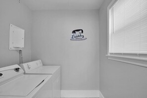 Un cuarto de lavado con una secadora de pared, una lavadora y una ventana con persianas.