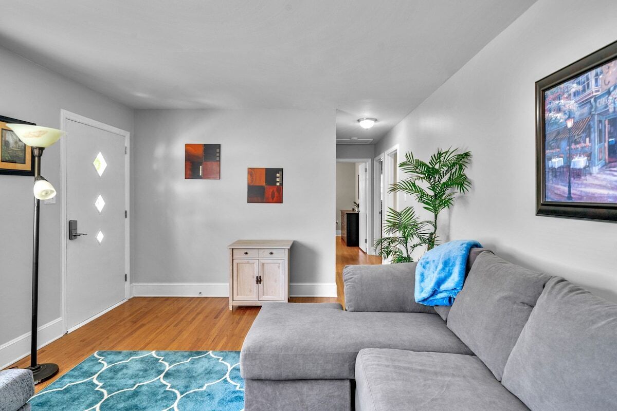 Ein modernes Wohnzimmer mit grauem Sofa, einem blau gemusterten Teppich, einer Stehlampe und einem Bild an der Wand.