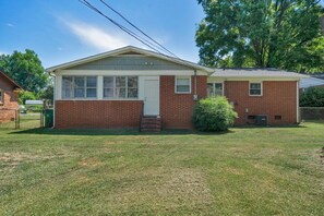A single-story brick house with a front porch, a small front yard, and a mailbox. - Cozy Pet Friendly Home with Private Backyard (Charlotte)