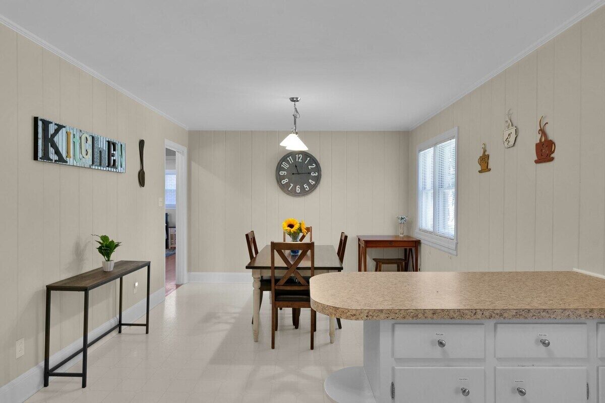 A kitchen with a dining area, a clock, and a window with blinds.