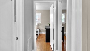 A hallway with a door on the left, a black cabinet in the center, and a window with blinds in the background. - Cozy Pet Friendly Home with Private Backyard (Charlotte)
