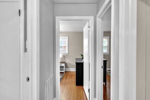 A hallway with a door on the left, a black cabinet in the center, and a window with blinds in the background. - Cozy Pet Friendly Home with Private Backyard (Charlotte)