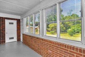 A hallway with a brick wall, a white door, and a window with blinds. - Pet-Friendly 2BR | Fenced Yard & Near Plaza Midwood (Charlotte)