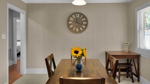 A dining area with a wooden table, chairs, a wall clock, and a vase with sunflowers. - Cozy Pet Friendly Home with Private Backyard (Charlotte)