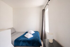 A hotel room with a bed, a blue blanket, and a bedside table with a lamp.