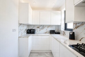 Een compacte keuken met witte kastjes, een marmeren achterwand en een gasfornuis.