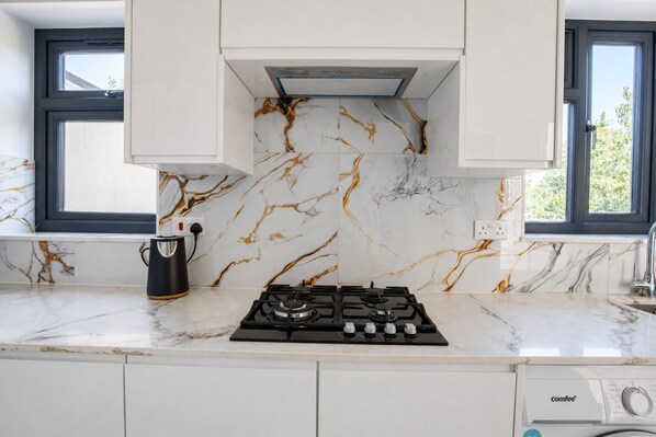 A modern kitchen with white cabinetry, a gas stove, a coffee maker, and marble backsplash.