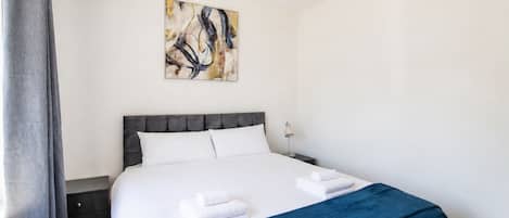 A hotel room with a bed, a nightstand, a lamp, and a painting on the wall.