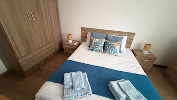 Habitación de hotel con una cama grande, armario de madera, mesitas de noche y colcha azul acolchada.