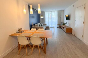Una sala moderna con comedor, un juego de sofá, televisor montado en la pared y puerta que da a otra habitación.