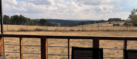 A wooden deck with a view of a grassy field and distant hills.