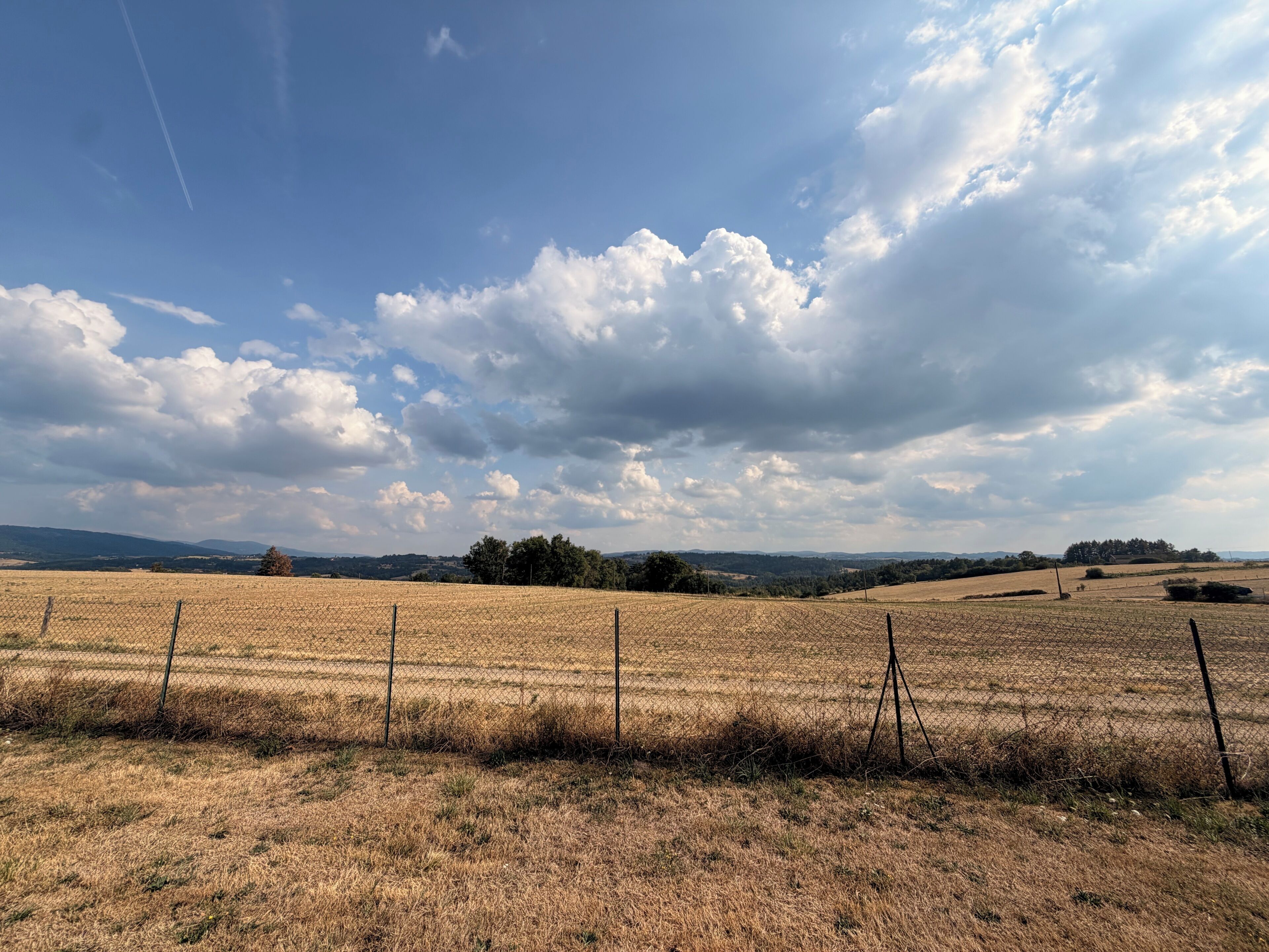 Paisaje rural con un campo, valla y colinas distantes.