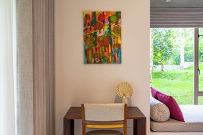 A room with a desk, a colorful abstract painting, a woven basket, and a view of greenery outside. - ONA Garden Villa: Deluxe Double Room (Galle)