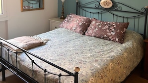 Ein Schlafzimmer mit einem Bett, einem Nachttisch, einem Spiegel und einer Wandblume.