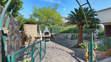 A stone pathway leading to a courtyard with a barbecue area, a bicycle, and a palm tree.