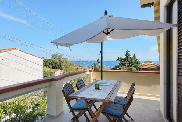 A balcony with a table and chairs, an umbrella, and a view of the sea.