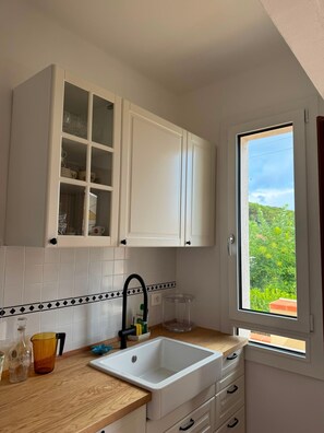 A kitchen with white cabinets, a sink, and a window with a view of greenery.