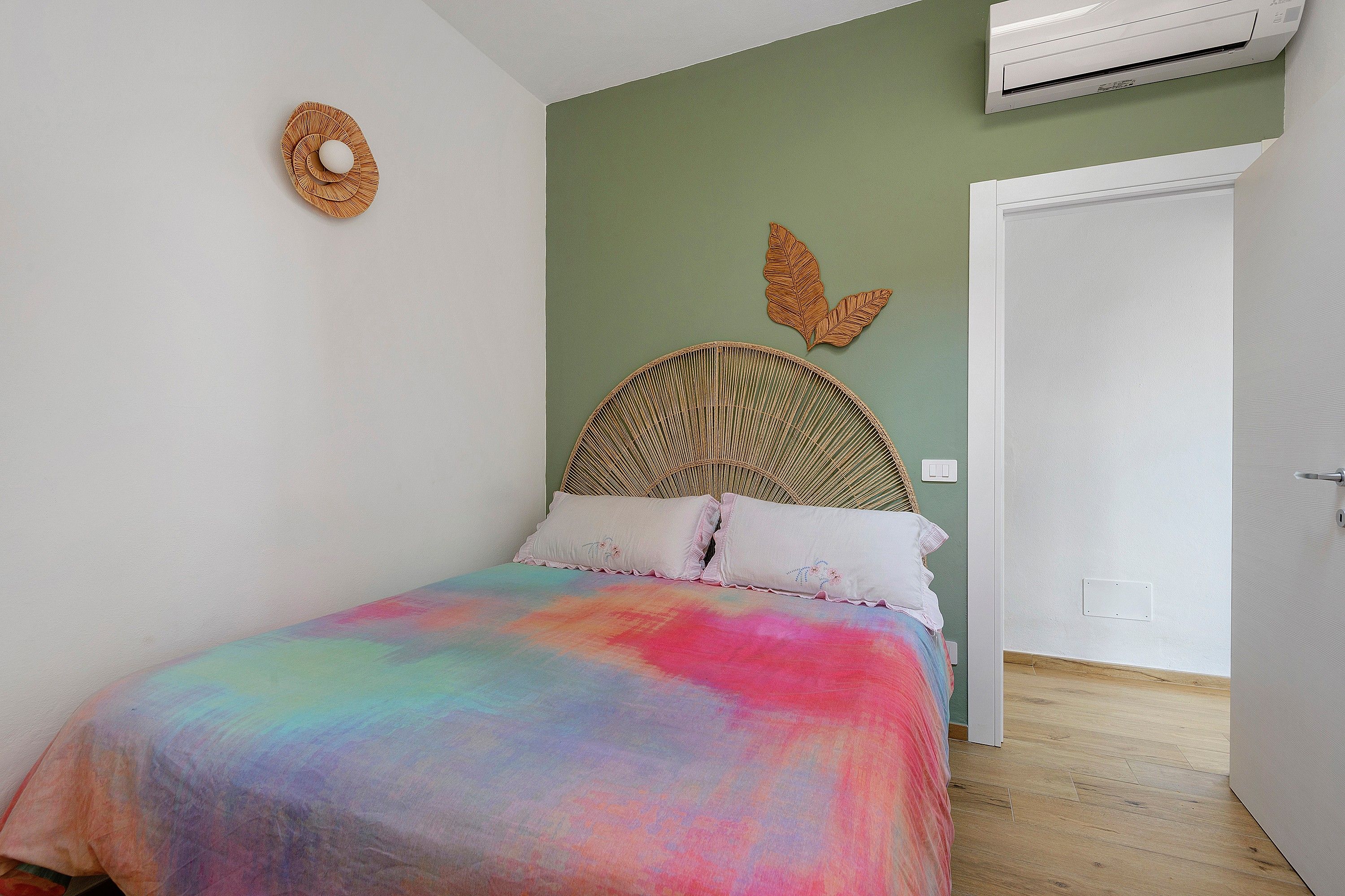 A bedroom with a bed, a wall-mounted air conditioner, a door, and a wall decoration.