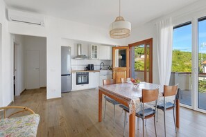 A modern kitchen with white cabinets, a stainless steel range hood, and a wooden dining table with chairs.