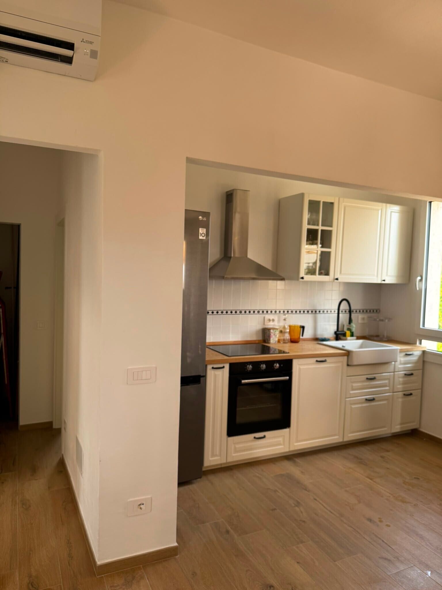 Una cocina moderna con gabinetes blancos, un extractor de acero inoxidable y un horno empotrado.