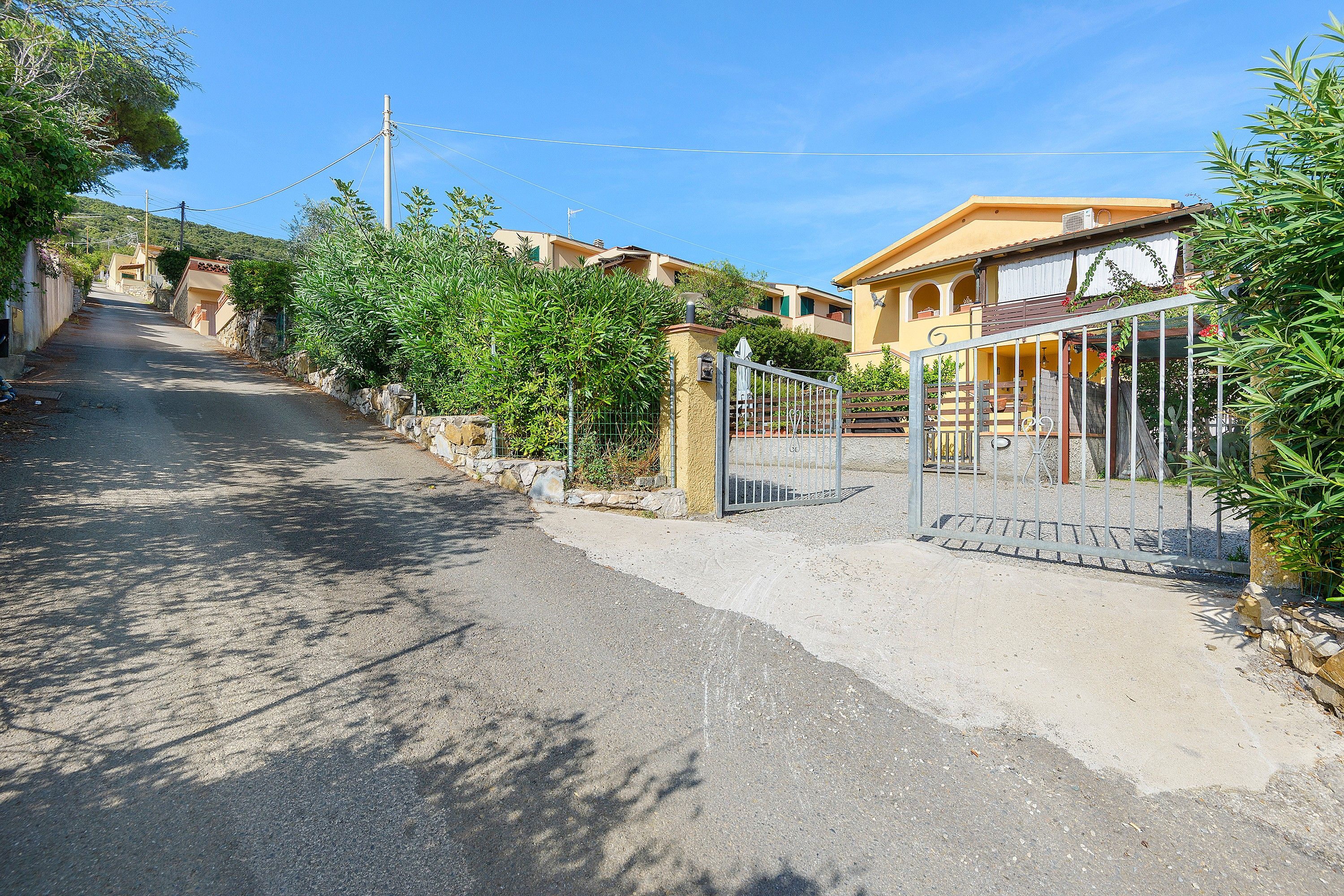 Une rue résidentielle bordée de maisons, avec une entrée sécurisée et un ciel dégagé.