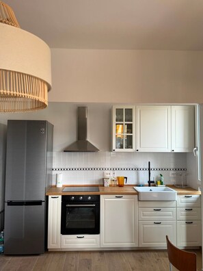 A modern kitchen with a stainless steel refrigerator, a built-in oven, a wooden countertop, white cabinets, and a pendant light.