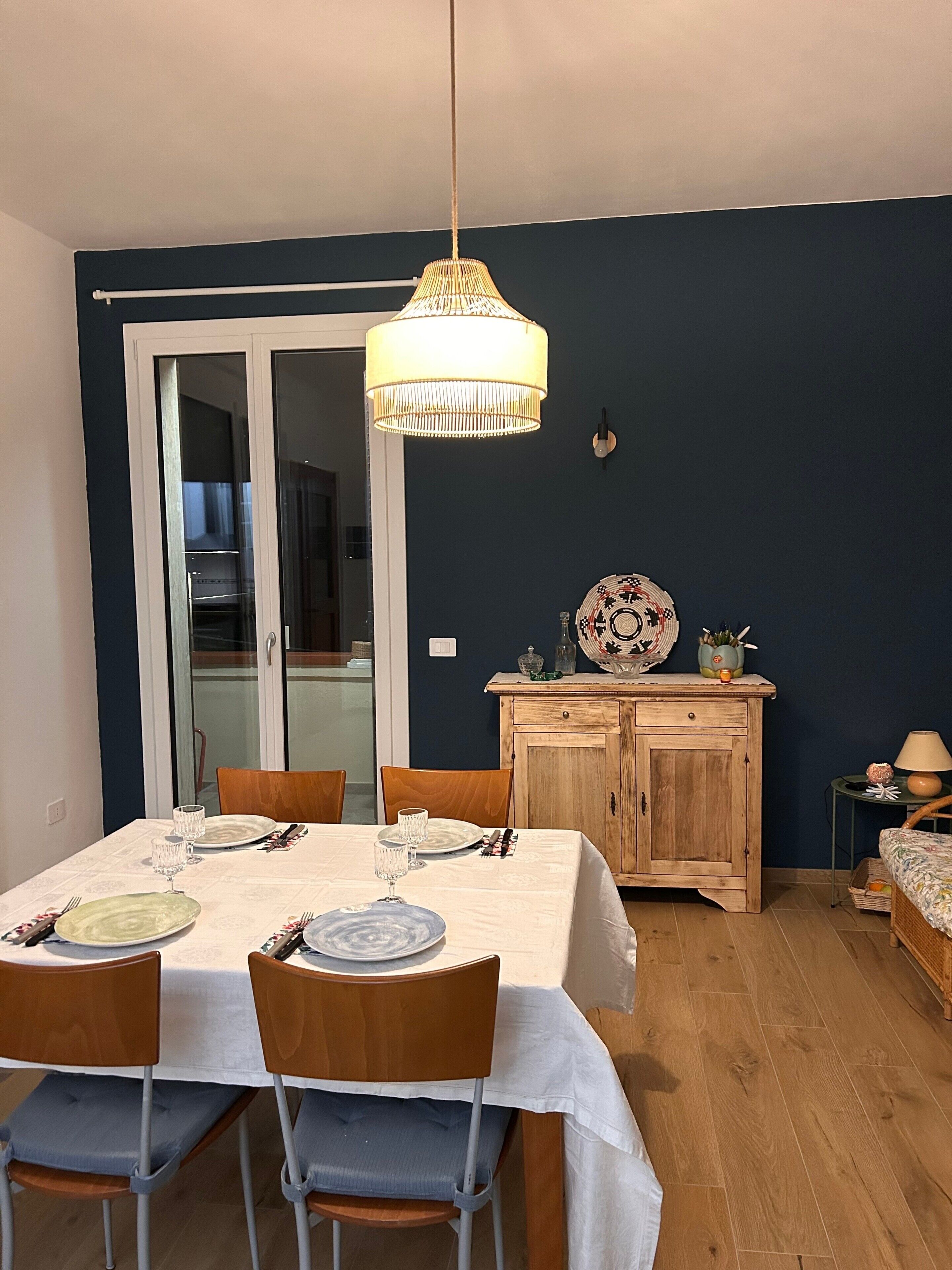 Comedor con una mesa dispuesta para cuatro, sillas, un aparador de madera y una lámpara colgante.